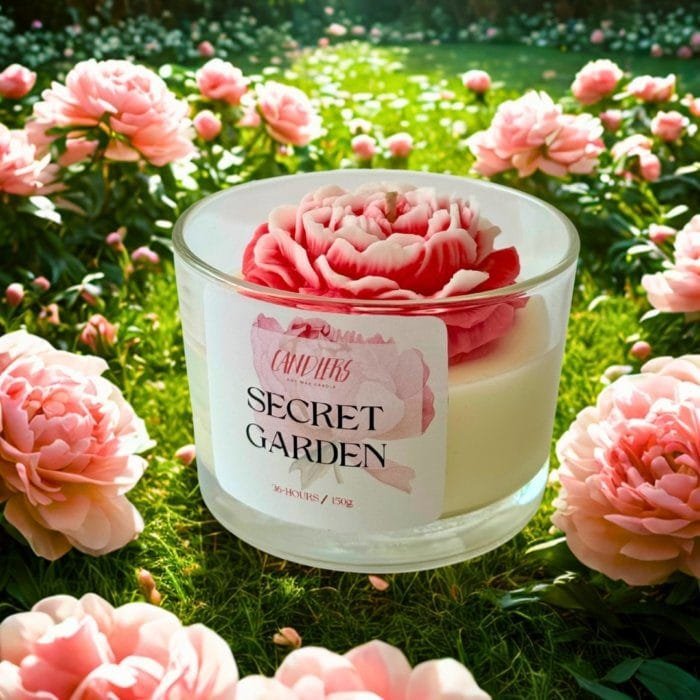 Χειροποίητο κερί σόγιας Secret Garden σε γυάλινο δοχείο 150gr, διακοσμημένο με ροζ και λευκή παιώνια, τοποθετημένο σε παραμυθένιο κήπο με ανθισμένες παιώνιες και ηλιόλουστο, αιθέριο φόντο.